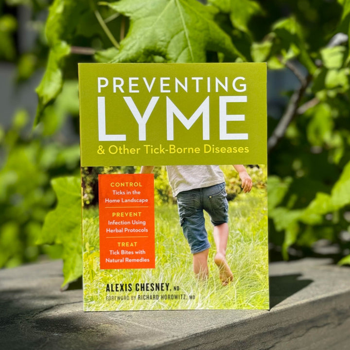 Book titled 'Preventing Lyme & Other Tick-Borne Diseases' by Alexis Chesney on a wooden surface with greenery in the background.