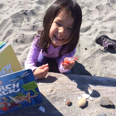 Child on a sandy beach with a book and shells
