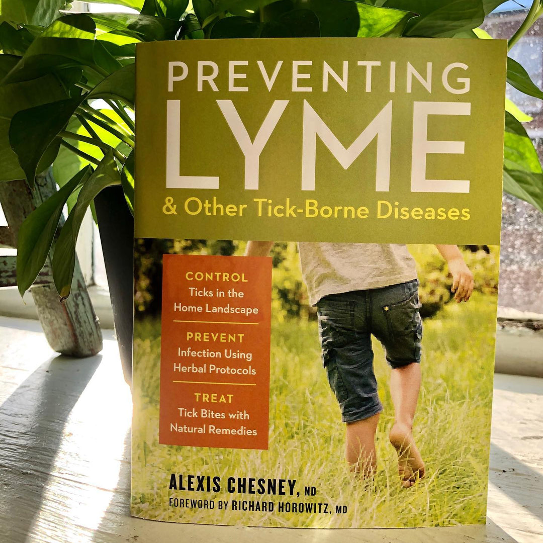 Book titled 'Preventing Lyme & Other Tick-Borne Diseases' by Alexis Chesney on a wooden surface with plants in the background.