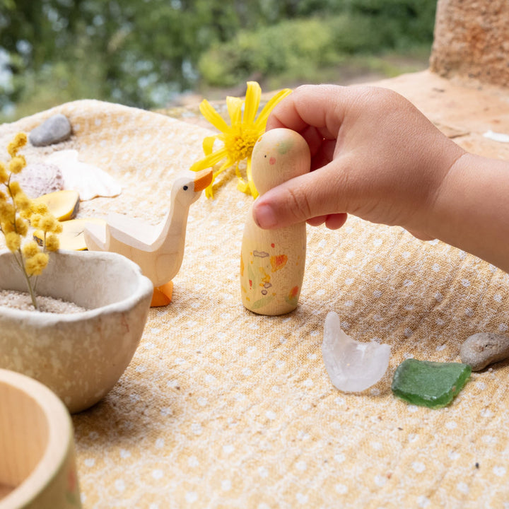 Hand holding a Grapat peg doll with a sand play scene featuring Ostheimer wooden goose.