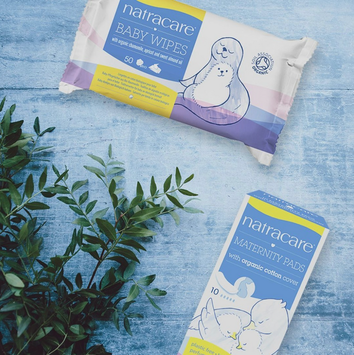 Natracare organic baby wipes & organic maternity pads pictured together with a leafy green plant.
