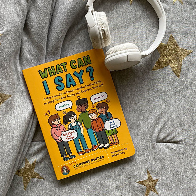 Book titled 'What Can I Say?' on a gray blanket with gold stars and white headphones.