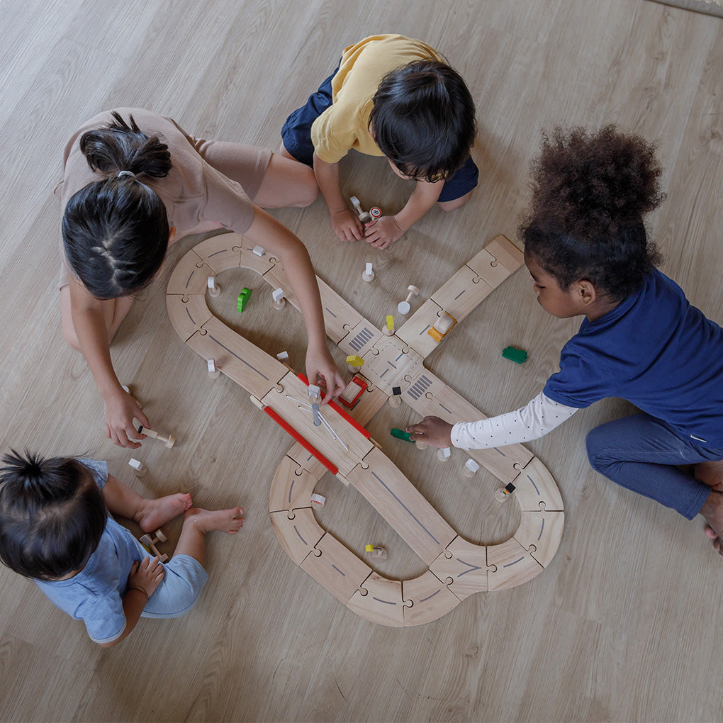 Children playing with a Plan Toys wooden toy track on a wooden floor
