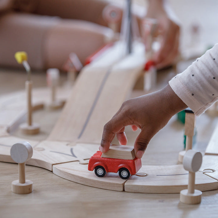 Child playing with a Plan Toys red toy wooden car on a wooden track