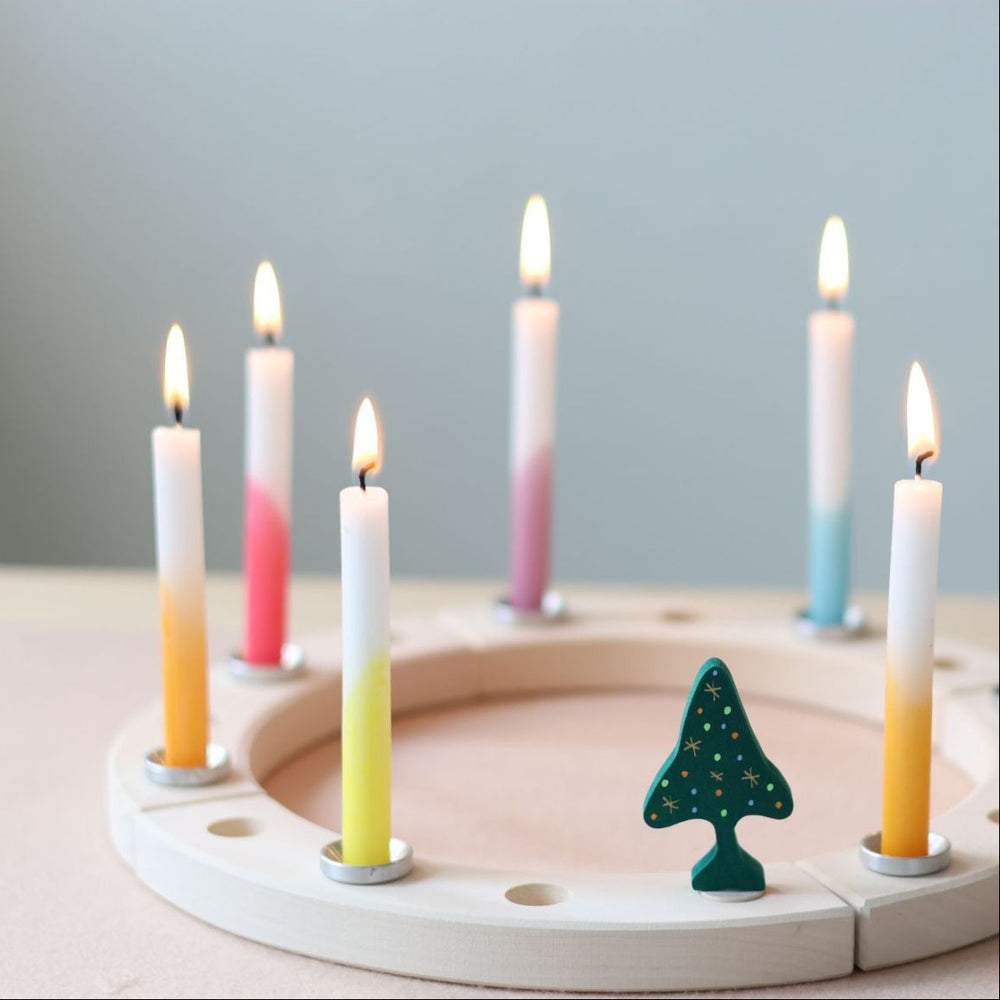 Wooden advent calendar with lit candles and a tree-shaped decoration on a light surface.