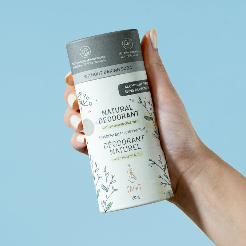 Hand holding a natural deodorant container against a light blue background