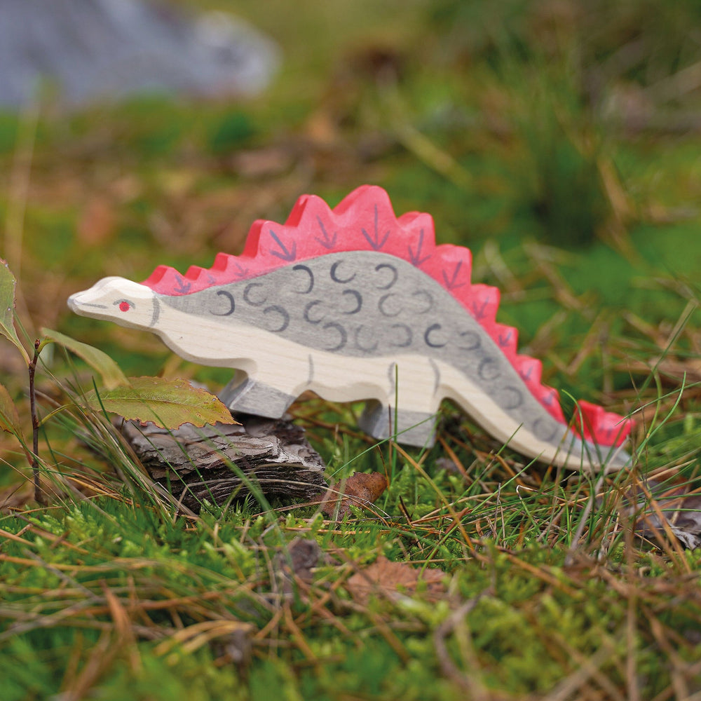 Holztiger stegosaurus wooden toy figurine outdoors in the grass with bark