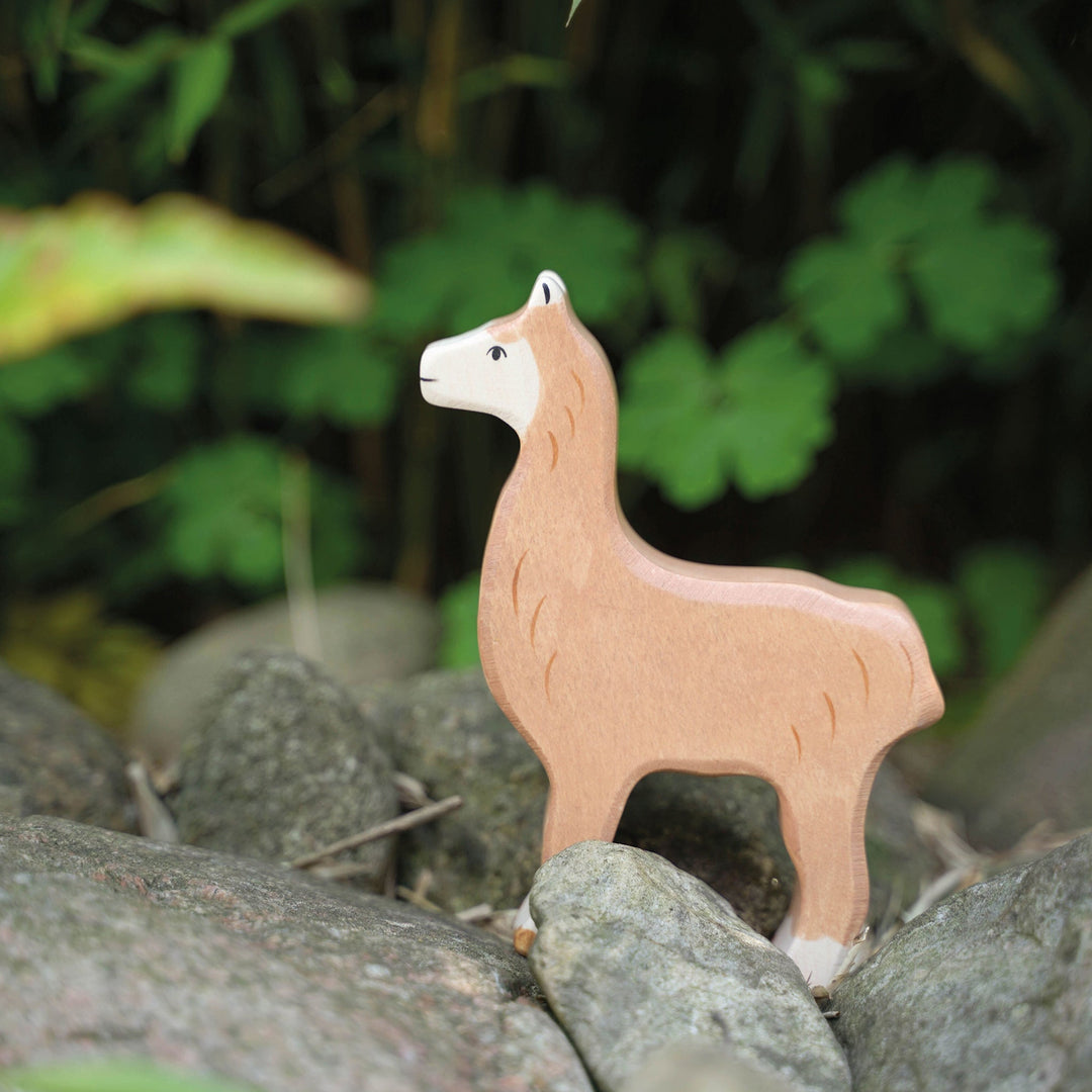 Holztiger brand wooden toy alpaca on rocks with a green leafy background