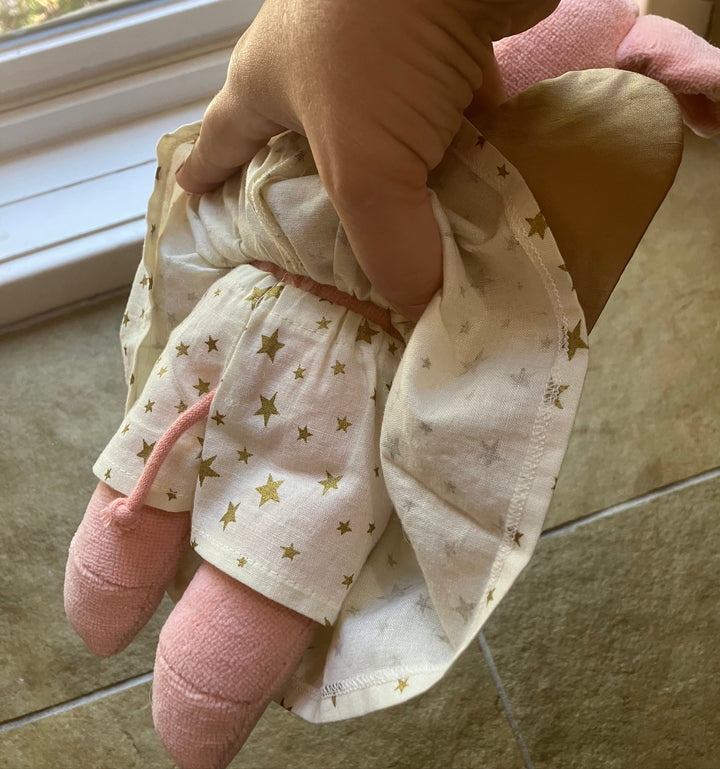 Organic wool and cotton plush pig by Senger from Germany in a white outfit with gold stars held by an adult on a tiled floor.