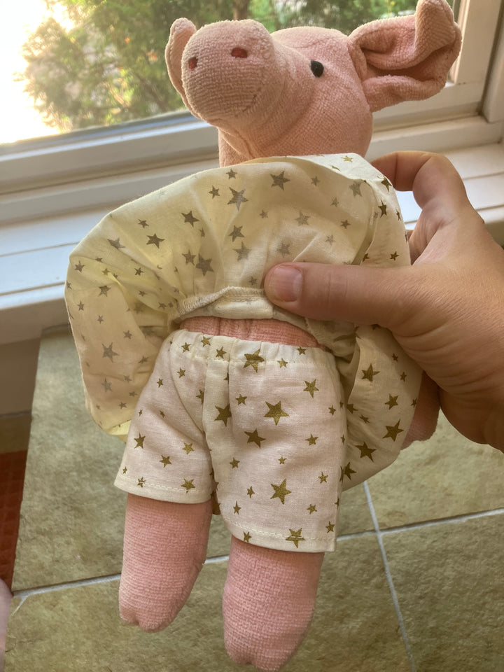 Hand holding a Senger pink pig plush toy with a star-patterned outfit on a tiled floor.
