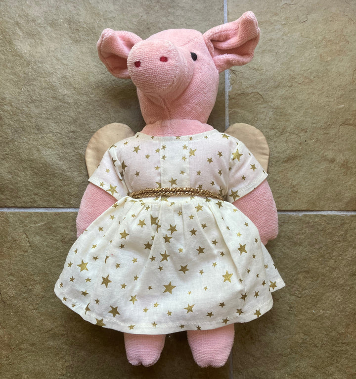 Pink stuffed animal wearing a white dress with gold stars on a tiled floor.