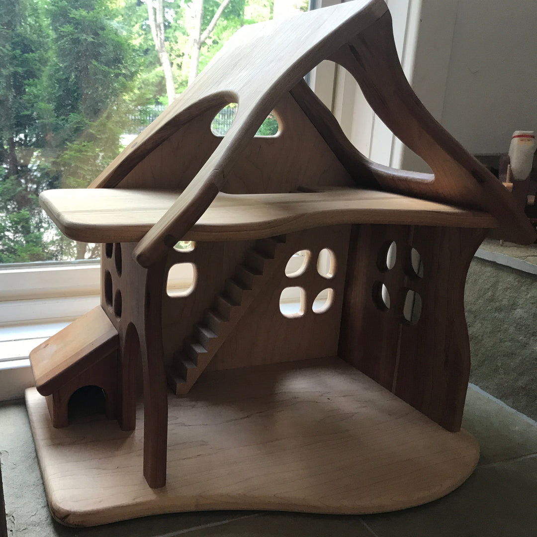 Camden Rose/ Palumba Wooden dollhouse made of solid cherry wood, in front of window with cedar tree in background.