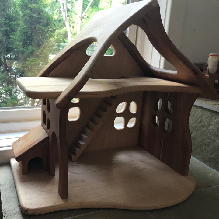 Camden Rose/ Palumba Wooden dollhouse made of solid cherry wood, in front of window with cedar tree in background.