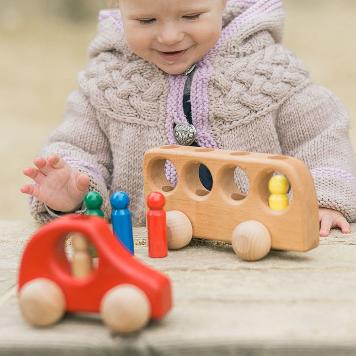 Toddler in chunky knit sweater with big heart button smiling at Ostheimer bus and red cat with peg people.