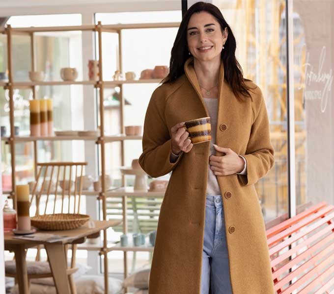 Woman in a beige coat holding a cup in a store setting with 'disana' branding.