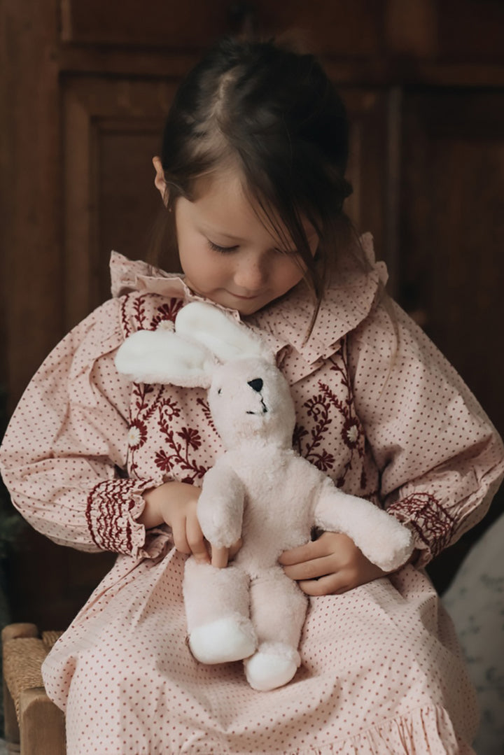 Young girl in a patterned dress holding an organic cotton and wool Senger grand light rose pink stuffed bunny.