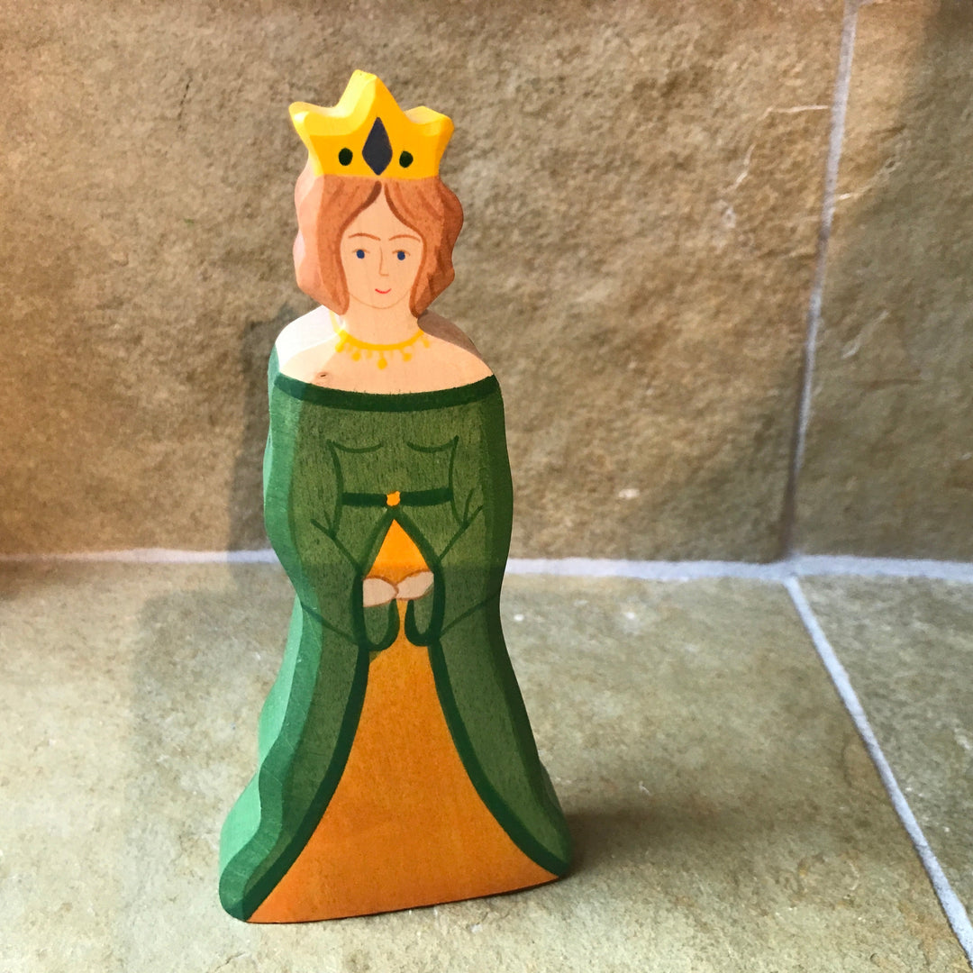 Wooden figurine of a character in a green dress and yellow crown on a stone floor.