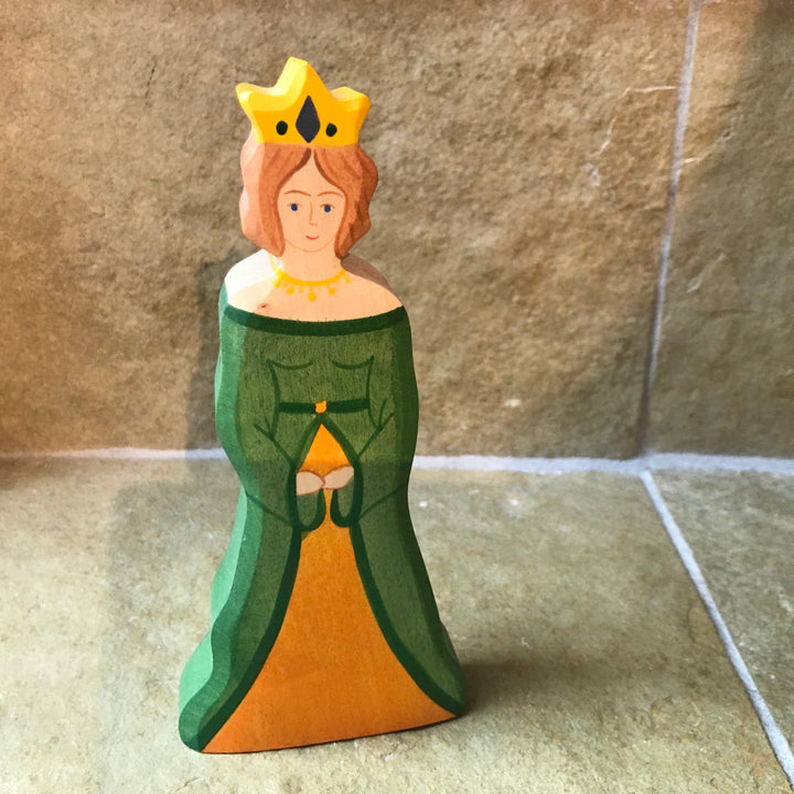 Wooden figurine of a character in a green dress and yellow crown on a stone floor.