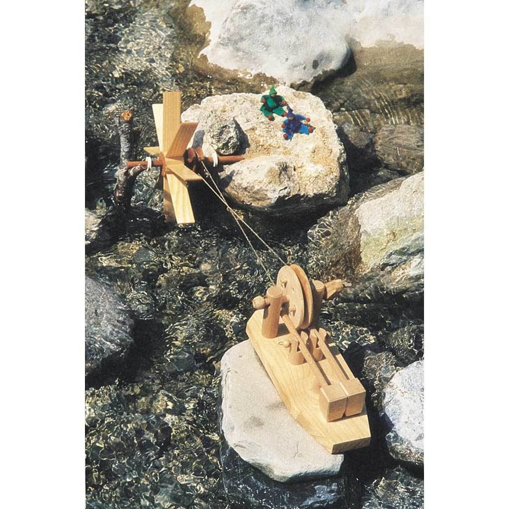 Small waterwheel powering hammermill kit to do physical work, on a river in the water, with large rocks.